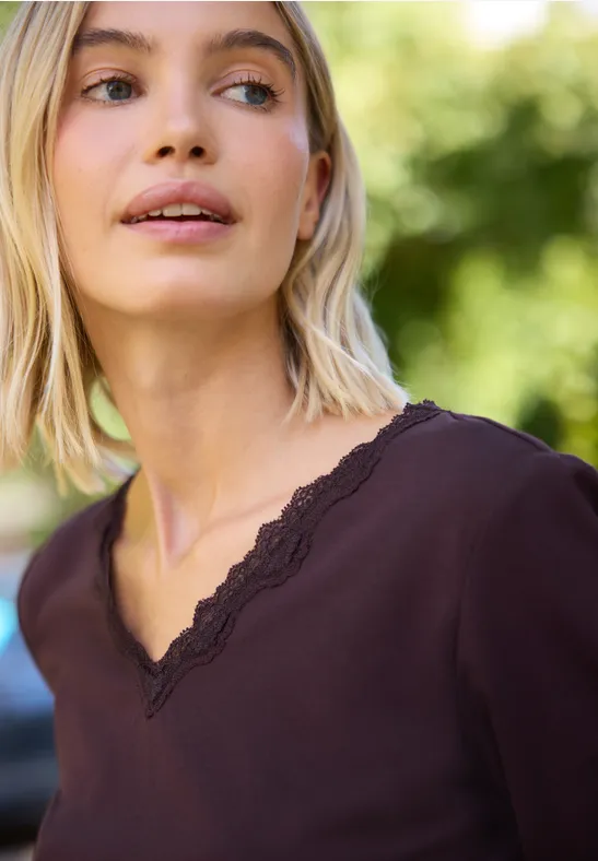 Blondine in donkerpaarse V-hals met kant kijkt buiten omhoog.