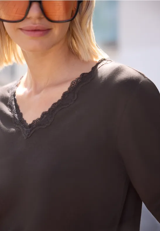 Vrouw met blond bobkapsel en zonnebril draagt een donker T-shirt met V-hals en kanten rand