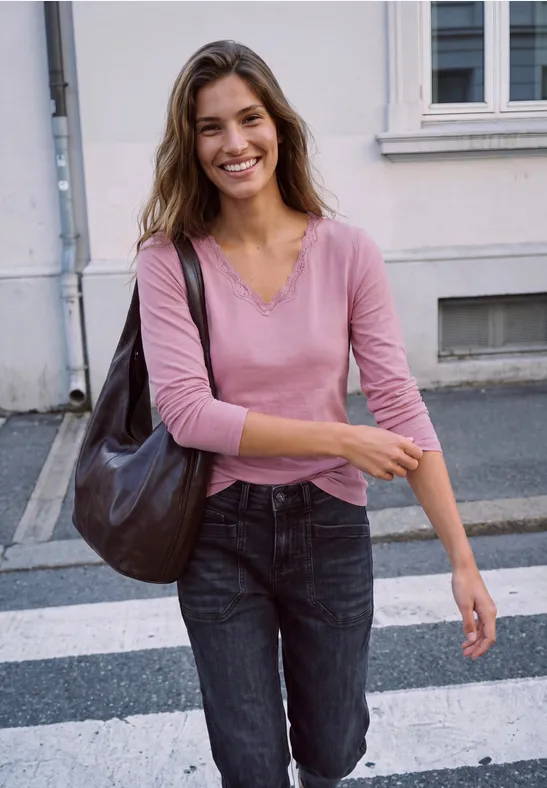 Eine fröhliche Frau in rosa Shirt und Jeans geht über einen Zebrastreifen und trägt eine große Tasche.