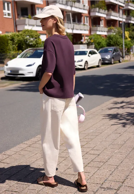Person in lila Shirt und weißer Hose mit Cap läuft auf dem Bürgersteig vor geparkten Autos und Wohnhäusern