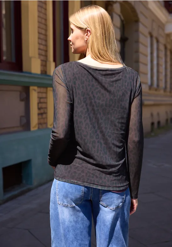 Frau von hinten, blondes Haar, schwarzer transparenter Langarmpullover und blaue Jeans, vor Gebäude in Straße.