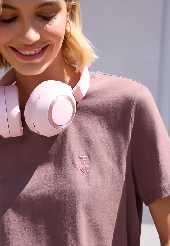 Person mit rosa Kopfhörern und T-Shirt mit kleinem Kirschlogo