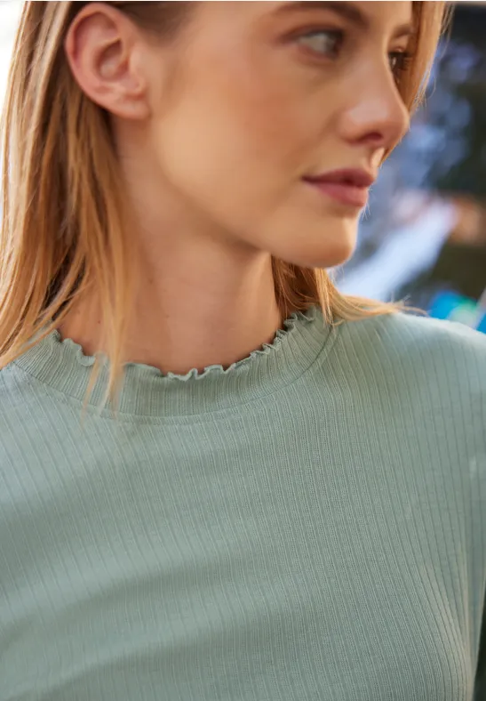 Seitliches Porträt einer jungen Frau mit hellgrünem Rippsweater und Rüschenkragen.