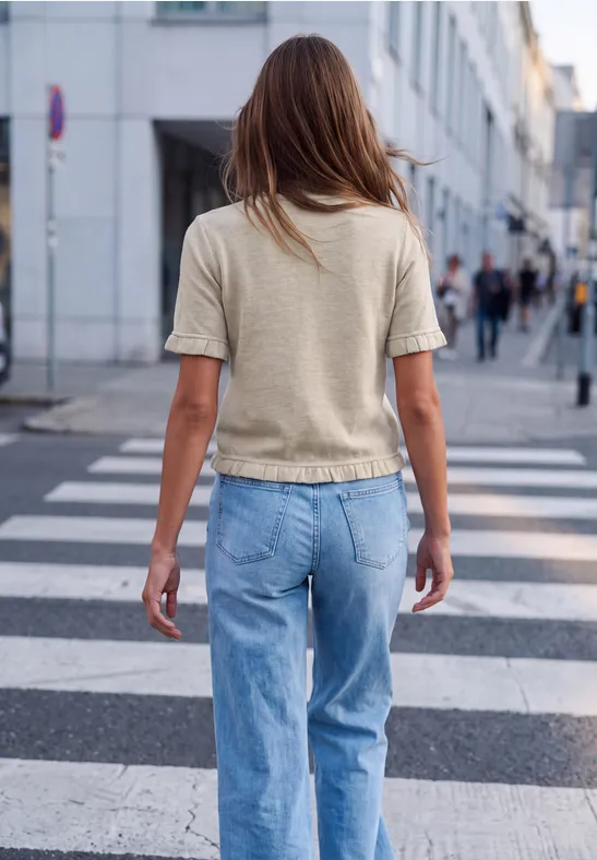Eine Frau in Jeans und T-Shirt geht über einen Zebrastreifen in der Stadt, seitliche Ansicht von hinten.
