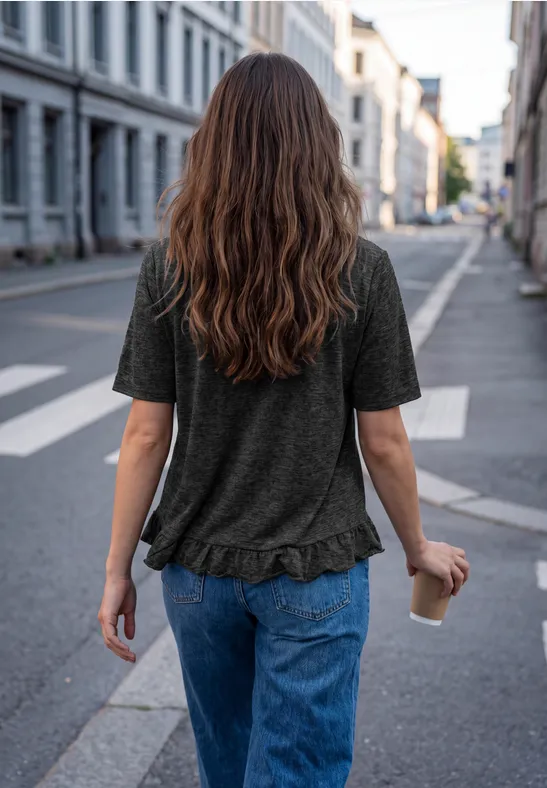 Eine Frau mit langen braunen Haaren geht in Jeans und T-Shirt mit Kaffee to go eine Straße entlang.