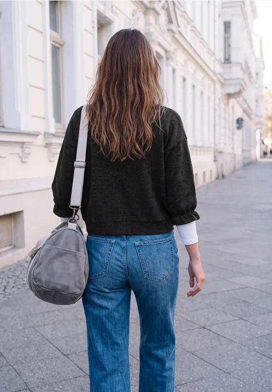 Eine Frau in blauer Jeans und schwarzem Pullover geht mit grauer Tasche eine Straße entlang.