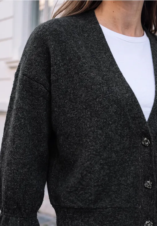 Eine Frau trägt einen dunkelgrauen Cardigan über weißem Shirt.