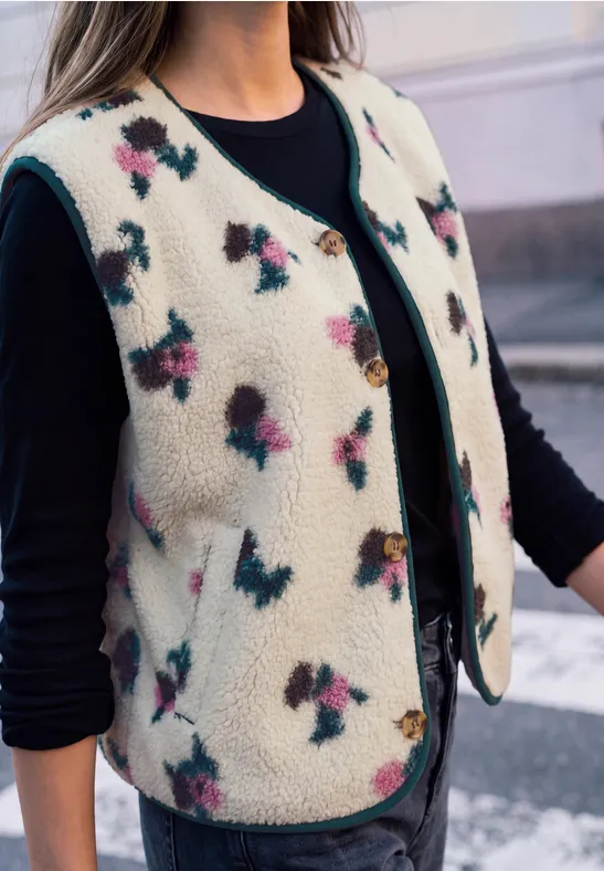 Personne porte un gilet polaire crème à fleurs colorées sur un t-shirt noir.