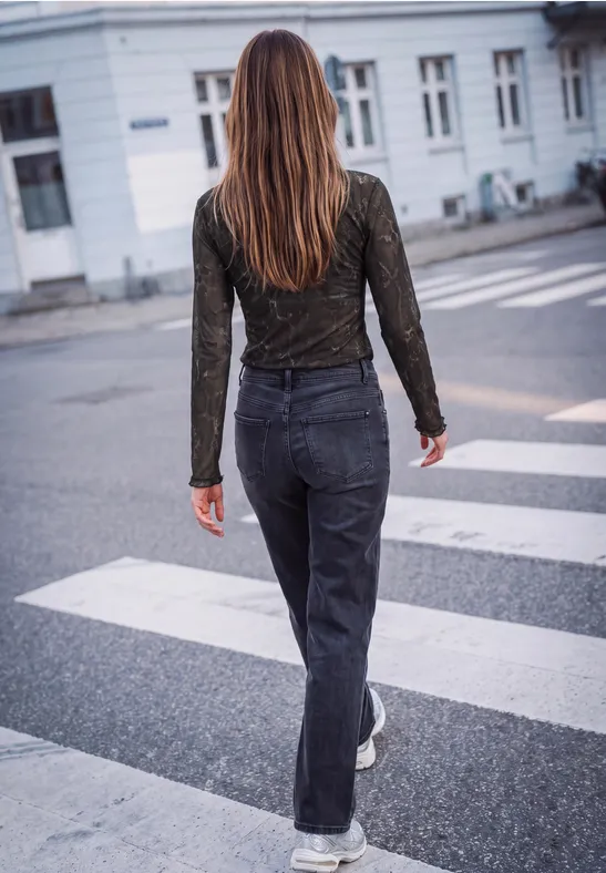 Een vrouw met lang haar loopt van achteren over een zebrapad in een donkere jeans en top in de stad.