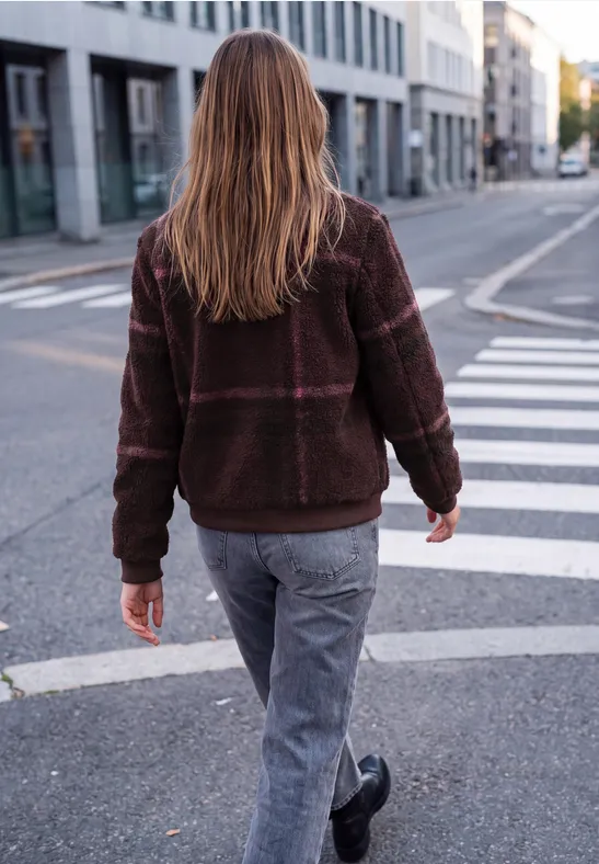 Eine Person in brauner Jacke und Jeans geht auf dem Zebrastreifen einer urbanen Straße.