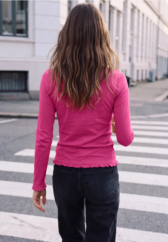 Een vrouw met lang haar en een roze trui loopt over een zebrapad de straat over.