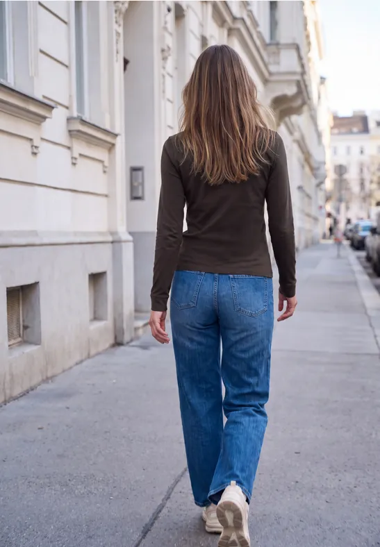 Frau in lässiger Kleidung läuft auf einem städtischen Gehweg mit Häuserfassaden im Hintergrund.