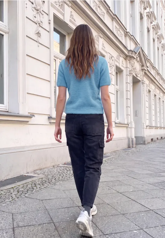 Eine Frau in blauem Pullover und schwarzer Hose geht an einer historischen Hausfassade entlang.