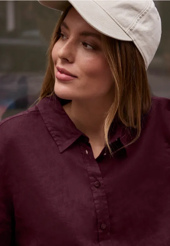 Personne portant une casquette blanche et une chemise rouge foncé, visage flou, arrière-plan indéfini.