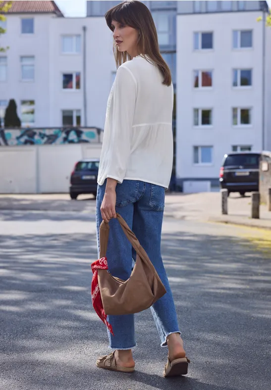 Vrouw van achteren op straat met wit hemd, blauwe jeans, sandalen en bruine tas met rood sjaaltje.