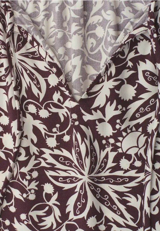 Nahaufnahme eines braun-beigen Stoffes mit symmetrischem Blumen- und Blattmuster.