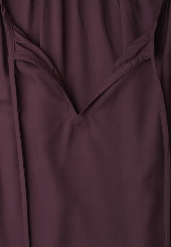 Close-up einer dunkelroten Hose mit sichtbarer Tasche und Nahtdetail.