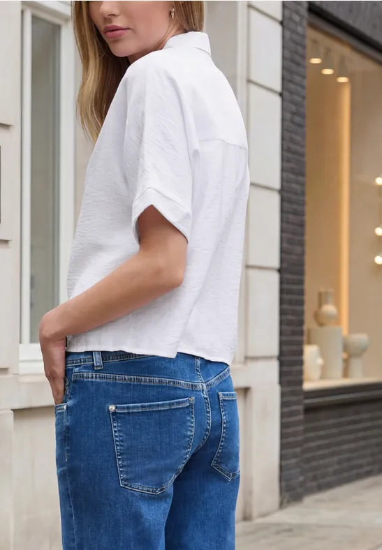 Frau mit weißem Hemd und blauen Jeans von der Seite auf der Straße.
