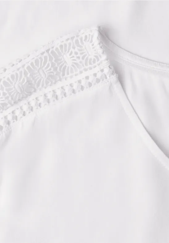 Haut blanc orné d'une fine dentelle à l'épaule.