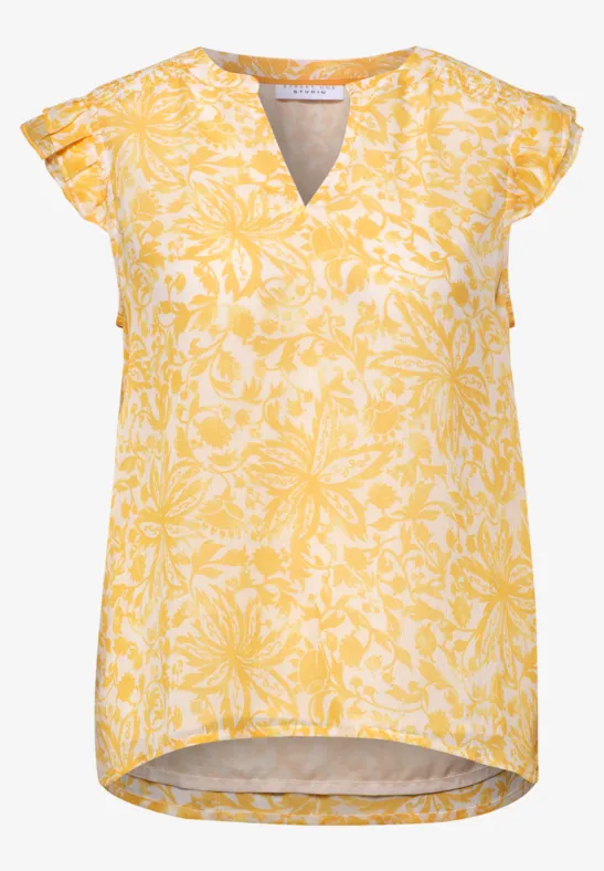 Gelbe Bluse mit weißem Blumenmuster, V-Ausschnitt und kurzen Flügelärmeln.