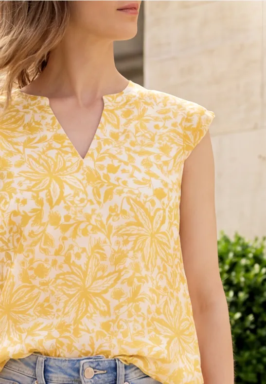 Frau im gelb-weißen, floralen Kurzarm-Top mit V-Ausschnitt, kombiniert mit blauer Jeans