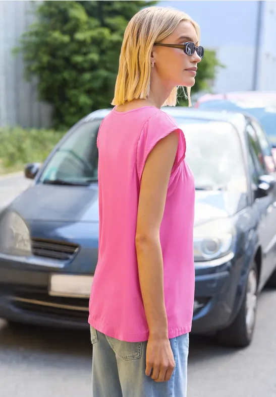 Een vrouw in een mouwloze roze top staat zijwaarts bij een geparkeerde auto op het voetpad.