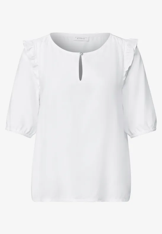 Weiße, feminine Bluse mit halblangen Ärmeln, Rüschen an den Schultern und kleinem Tropfenausschnitt.