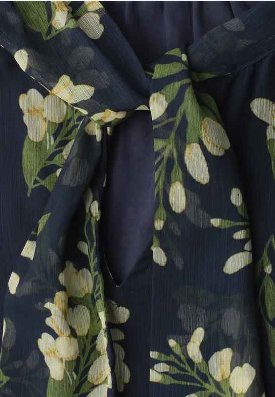 Dunkelblauer Stoff mit gelbweißen Blumen und grünen Blättern, Detail eines Oberteils mit Schlitz und Knoten.