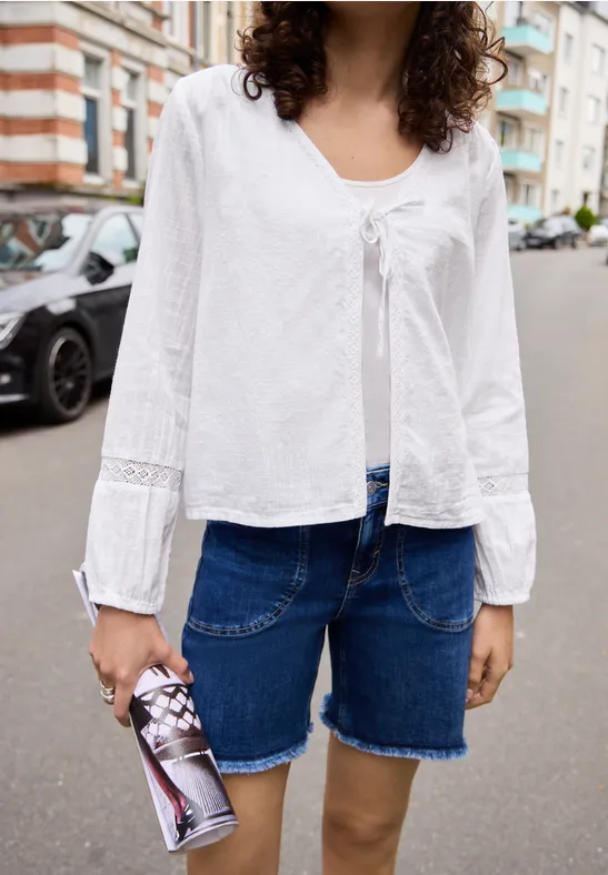 Person mit weißer Bluse und Jeans-Bermuda hält Getränkedose auf städtischer Straße.