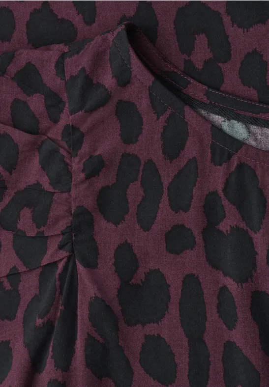 Nahaufnahme eines weinroten Stoffs mit schwarzem Leopardenmuster und Falten-/Taschendetail