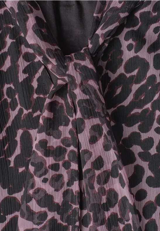 Close-up van een blouse met paars-zwarte luipaardprint en een decoratieve strik bij de kraag.