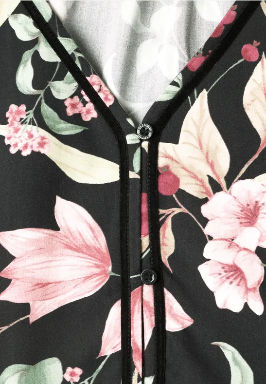 Schwarze Bluse mit V-Ausschnitt, zarten rosa Blumen und weißen Blättern, betont durch schwarze Paspelierungen.