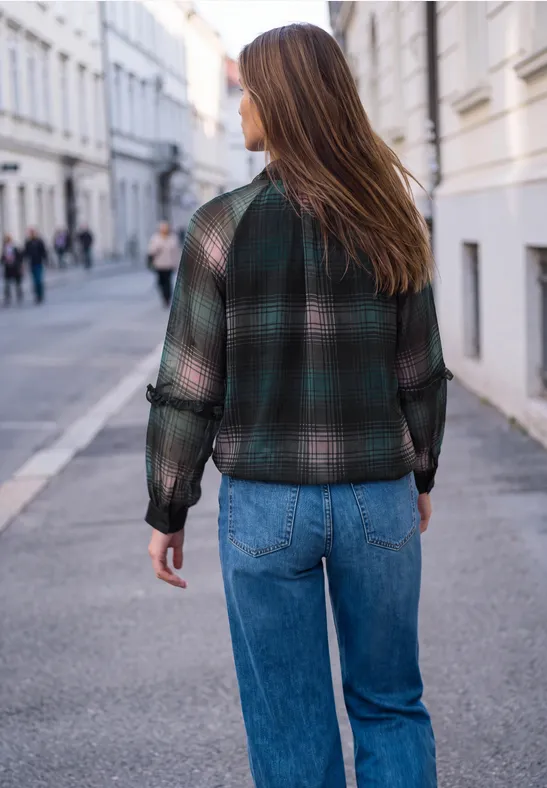 Eine Frau geht eine ruhige Stadtstraße entlang, trägt einen karierten Blouson und Jeans.