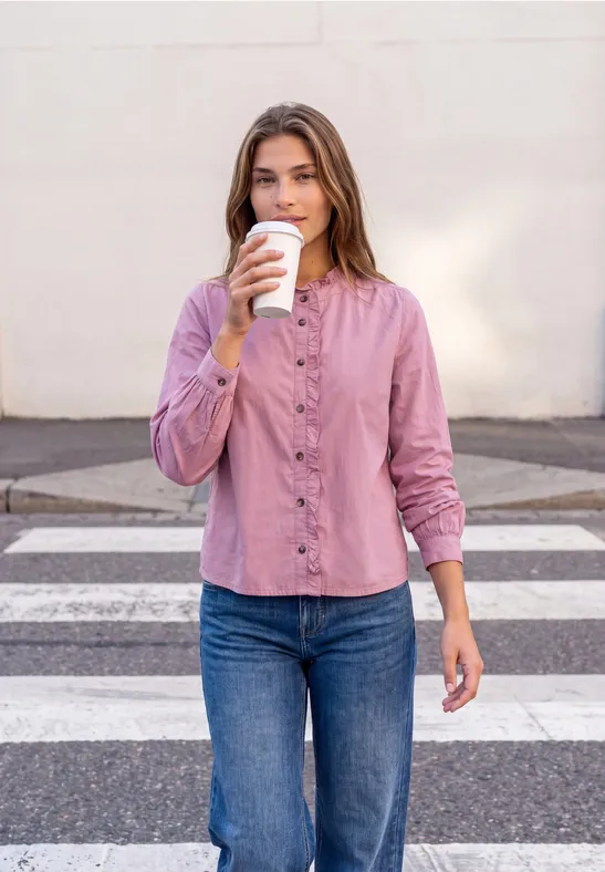 Frau in rosa Bluse und Jeans trinkt Coffee-to-go beim Überqueren eines Zebrastreifens.