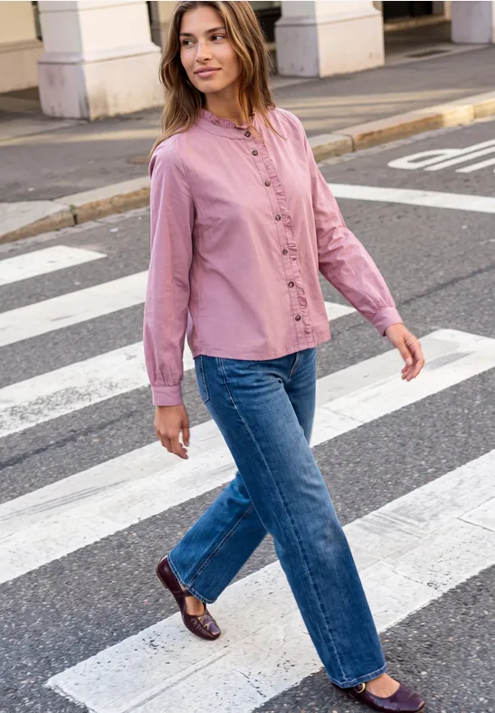 Frau in rosa Bluse, blauen Jeans und braunen Schuhen geht über Zebrastreifen.