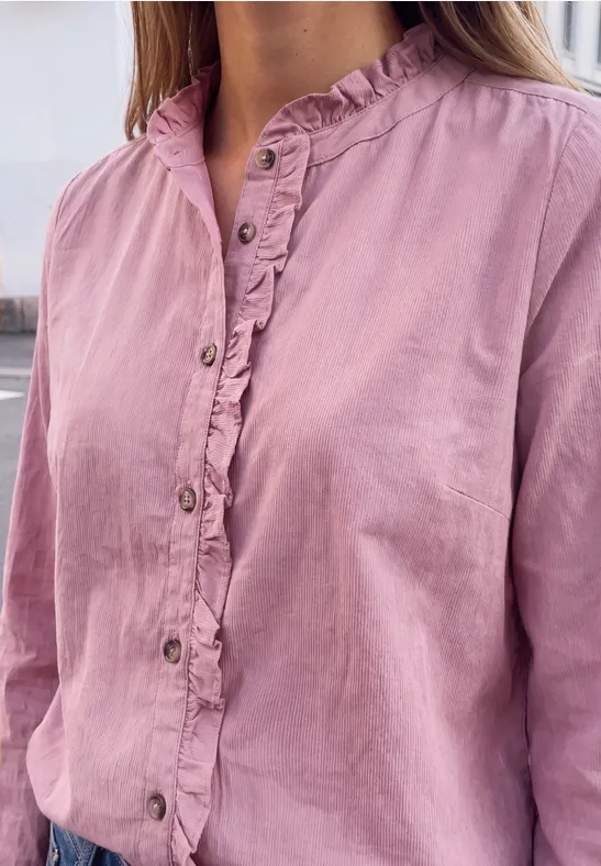 Eine Person trägt eine rosa Bluse mit Rüschen am Kragen und Knopfleiste.