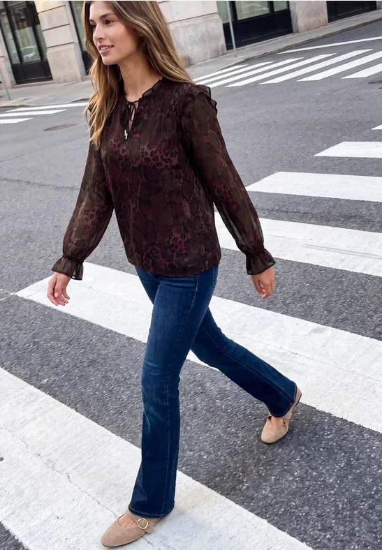 Frau in transparenter Spitzenbluse und Jeans überquert einen Zebrastreifen in der Stadt.
