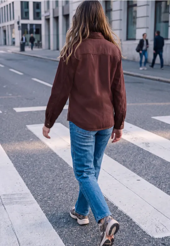 Eine Person mit braunem Hemd und blonden Haaren geht über einen Zebrastreifen in der Stadt.
