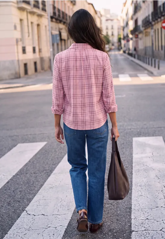 Eine Person in rosa Hemd und Jeans überquert einen Zebrastreifen und trägt eine Tasche.