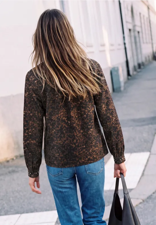Frau geht von hinten aufgenommen in Jeans und gemustertem Cardigan eine Straße entlang, Handtasche tragend
