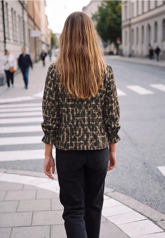 Eine Person mit langen Haaren und gemusterter Jacke läuft über einen Zebrastreifen in der Stadt.