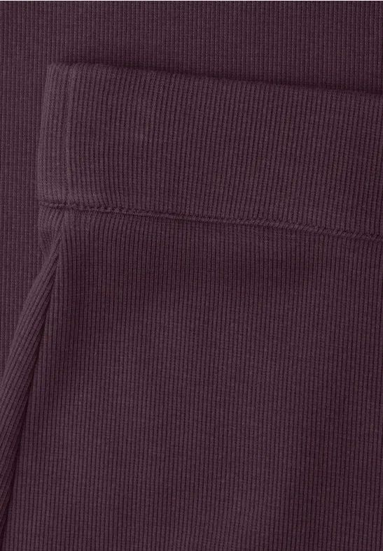 Close-up van een donkerpaars kledingstuk met geribbelde boord en zak.