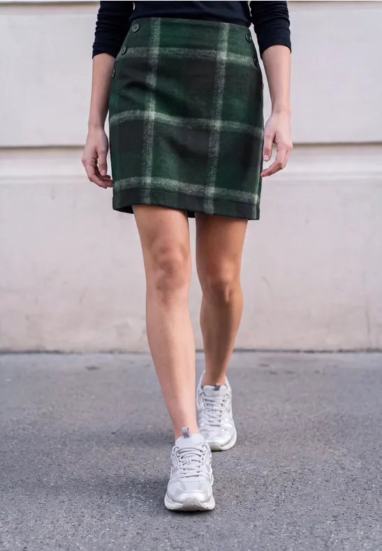 Vrouw in groene ruitrok en witte sneakers loopt over straat
