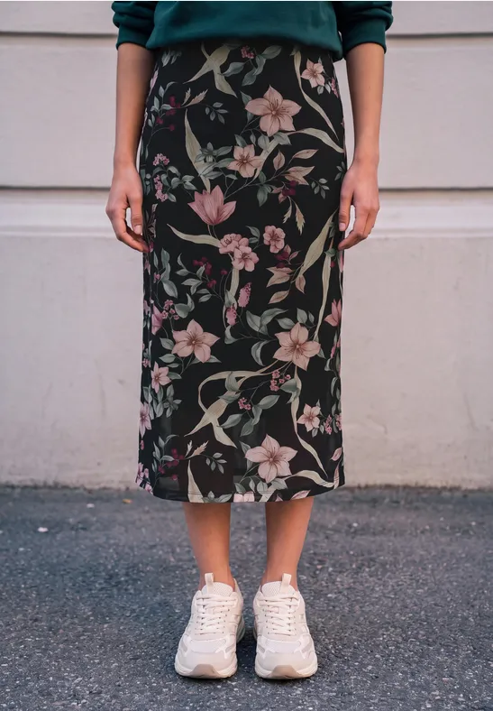 Eine Person trägt einen schwarzen, knöchellangen Rock mit rosa Blumenmuster und weiße Sneaker.