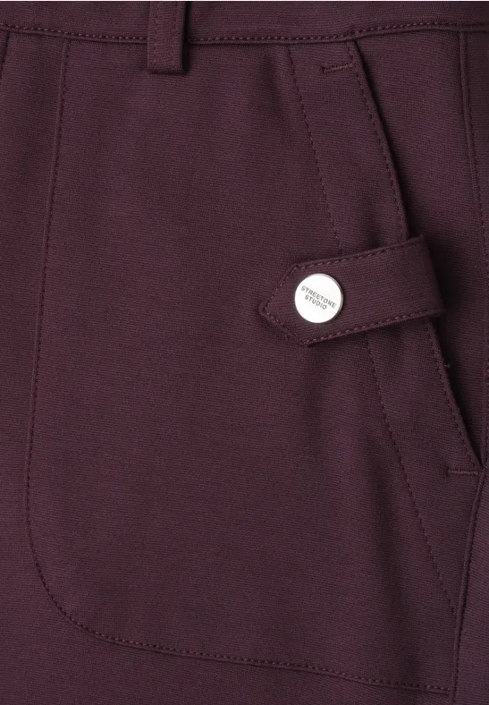 Poche latérale d’un vêtement violet foncé avec patte décorative et bouton en métal.