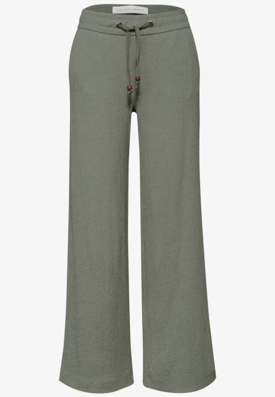 Pantalon fluide en lin vert olive, taille ajustable par cordon, coupe ample et confortable.
