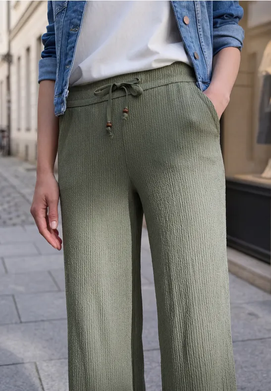 Pantalon large en tissu côtelé olive à cordon, porté avec un t-shirt blanc et une veste en jean.