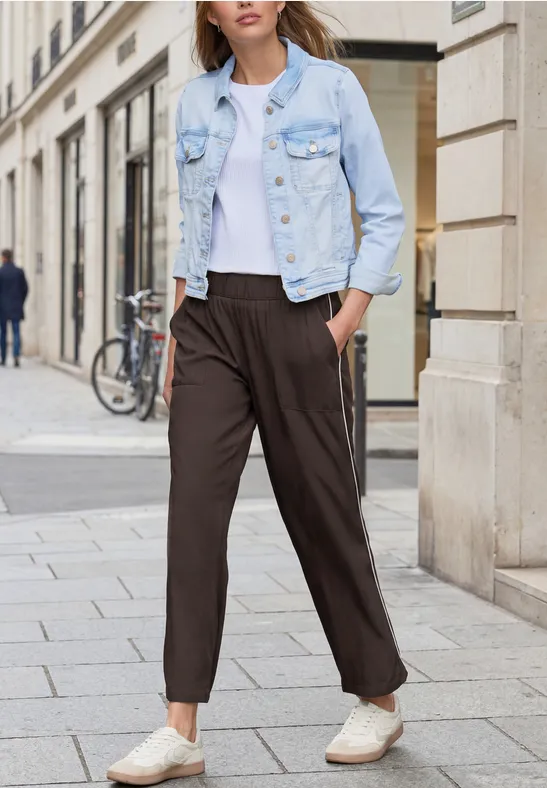 Person läuft in weißem T-Shirt, heller Jeansjacke und dunkler, lässiger Hose auf der Straße.