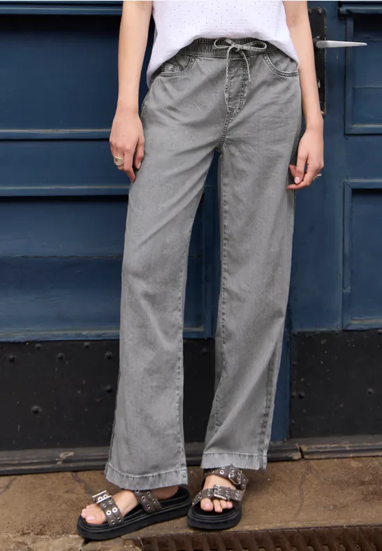 Graue, weite Hose mit Kordelzug und schwarze Sandalen vor einer blauen Tür.