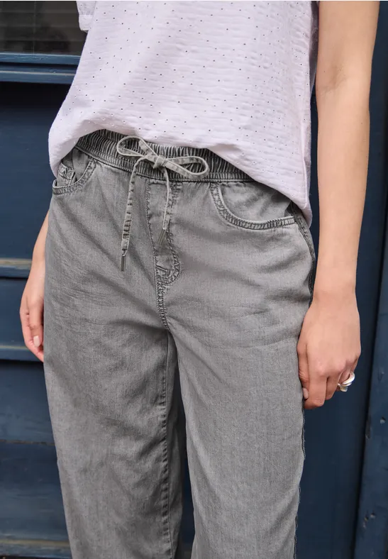 Graue Jeanshose mit Kordelzug an der Taille, kombiniert mit einer hellen Bluse.